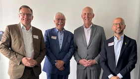 Four men in suits smile into the camera.