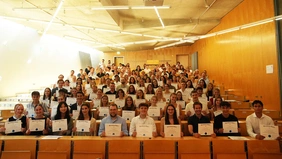 Ein voll besetzter Hörsaal mit Personen, die ihre Urkunden präsentieren.