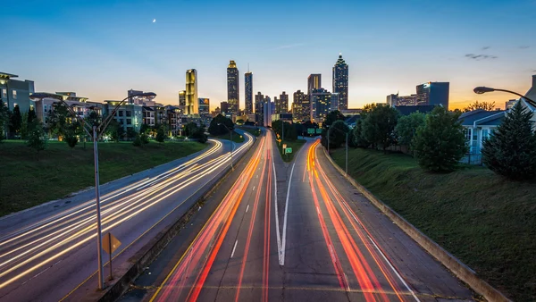 Eine mehrspurige Straße mit bunten Strichen durchzogen im Vordergrund, die Skyline einer Stadt im Hintergrund