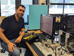 Mühenad Bilal im Labor (Foto: THI). mann an einem Schreibtisch, der mit einem Set aus verschiedenen Bohrern vor einem Bildschirm sitzt, neben ihm eine Bohrvorrichtung