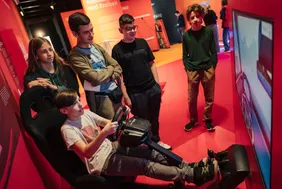 Wissenschaft erleben: Besucherinnen und Besucher testen das Exponat (© Foto: Ilja C. Hendel/Wissenschaft im Dialog). Junge Besucher des MS-Wisschenschaft Science Center, die an und um eine Fahrsimulation sitzen