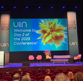 Source: THI Photo of the stage with the presentation in the background, which reads: UIIN Welcome to Day 2 of the 2025 Conference!
