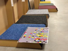 Puzzlearbeit für die Parkettleger: Der Boden des Raums ist nach einem speziellem Konzept gestaltet (Foto: THI). Kartons mit Teppichelementen in unterschiedlichen Farben und einem entsprechenden Anordnungsplan