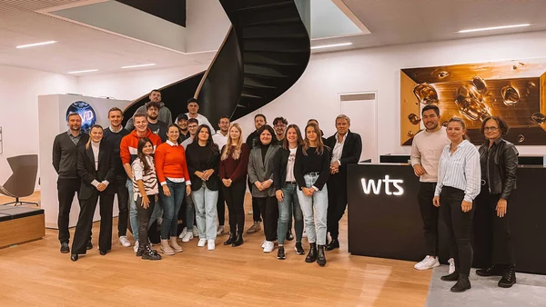 Eine Gruppe von 24 Menschen im modern gestalteten Eingangsbereich von WTS Advisory.