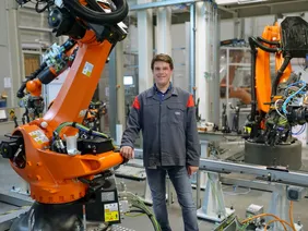 Vereint Theorie und Praxis: Professor Philipp Tröber (Foto: Audi). Professor Tröber stehend neben einem Fertigungsroboter in den Hallen der Audi AG