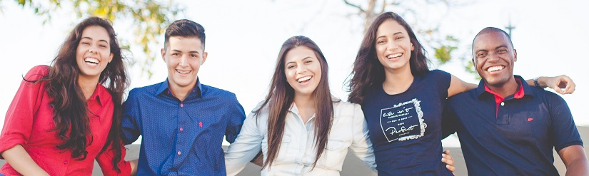 Five students stand arm in arm next to each other and laugh