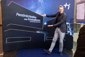 Prominenter Gratulant: Staatsminister Markus Blume lobte den Erfolg und die Dynamik der THI (Foto: THI). Stattsminister Blume vor einer Leinwand mit der Architektur der THI