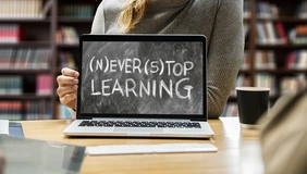 Symbolbild mit Laptop und Person dahinter, Auf dem Bildschirm steht: (N)ever (S)top Learning