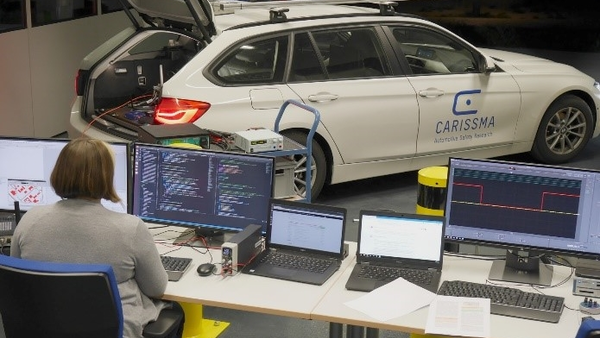 Image of a woman sitting in front of two screens. On which system tests of applications based on Car2X communication are running