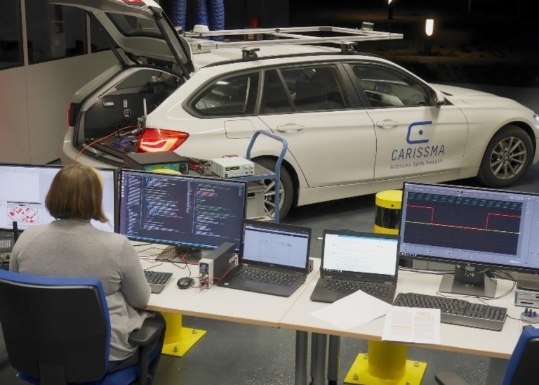 Abbildung einer Frau, die vor zwei Bildschirmen sitzt. Auf denen Systemtests von Anwendungen laufen, die auf Car2X-Kommunikation basieren