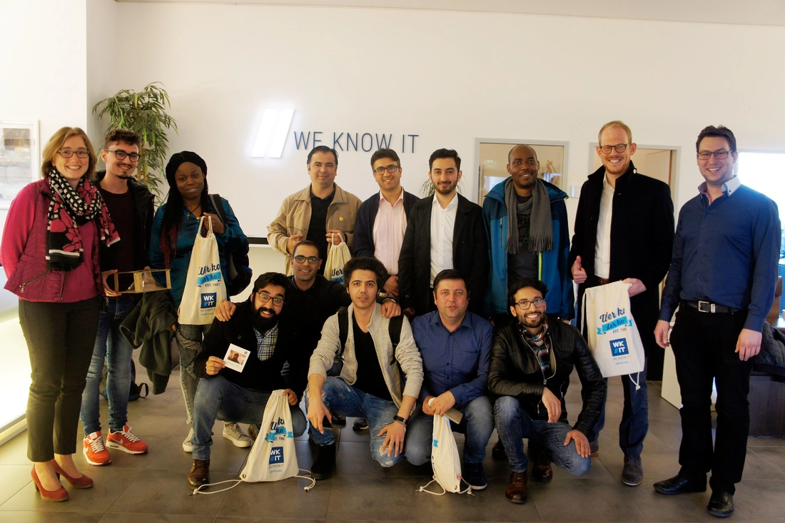 Blick in die Praxis: Die Teilnehmer zu Besuch bei WK IT in Ingolstadt. Quelle: WK IT GmbH Menschen vor Wand zum Gruppenfoto