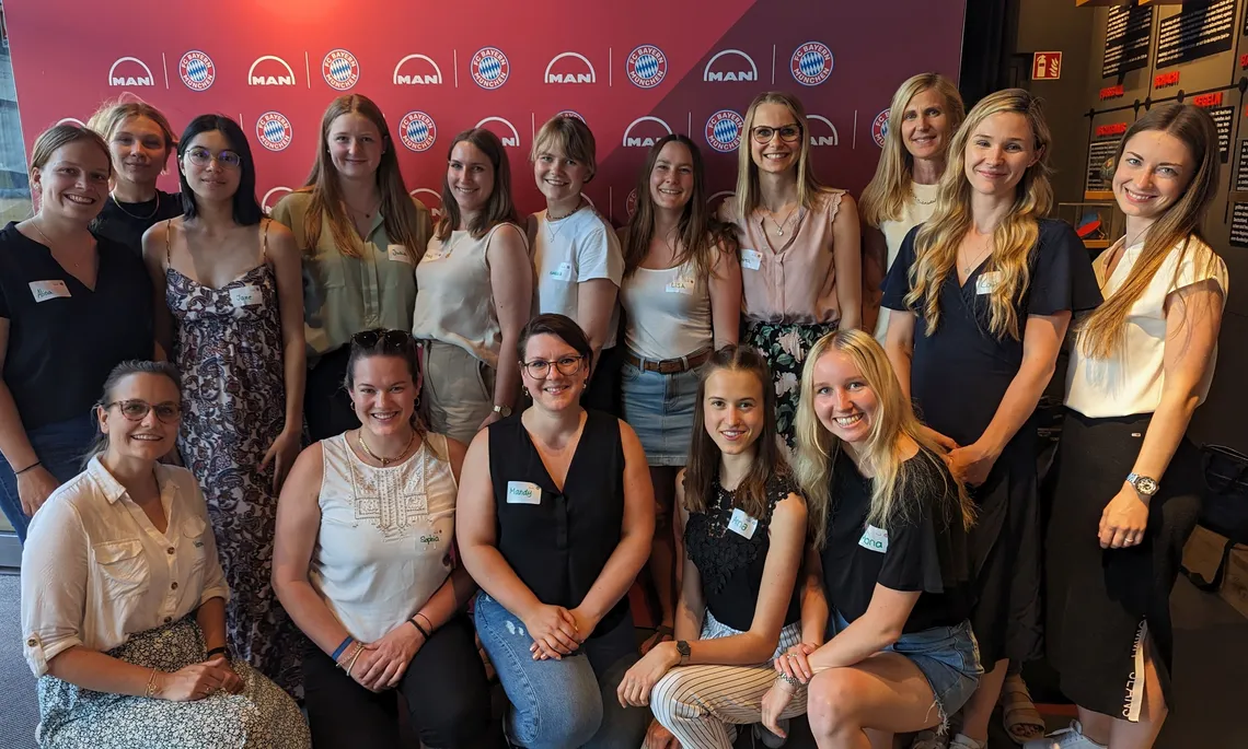 BayernMentoring-Teilnehmerinnen der THI und HS München platzieren sich vor der MAN und FC Bayern-Wand 