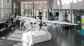 Einblick in das Urban Air Mobility Treffen in der Aula der THI, zusehen sind Ausstellungsmodelle sowie Gastgeber und Teilnehmer