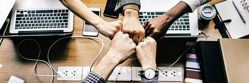 Fünf Fäuste treffen sich in der Mitte, im Hintergrund Laptops