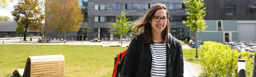 A female student is standing on campus in front of a THI building