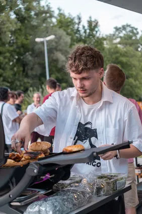 Für den Hunger nach den Präsentationen gab es Burger und Drinks (Foto: Maximilian Schütze). Portrait eines Studenten am Grill bei der Pecha Kucha Night