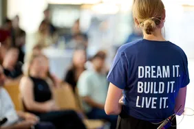 Bild einer Person mit Thirt, dass das Moto des CoE als Print auf dem Rücken hat: "Dream it. Built it. Live it."