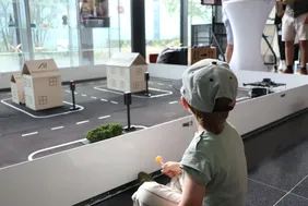 Der TurtleBot des AImotion Bavaria Instituts in Aktion (Foto: THI). Kleines Kind sitzend auf dem Boden vor dem Modell des TurtleBot