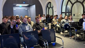 A group of people are sitting in a room with chairs.